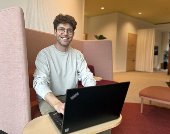 Student arbeitet in moderner Sitzecke im dmTECH-Unternehmenssitz und lächelt in die Kamera.