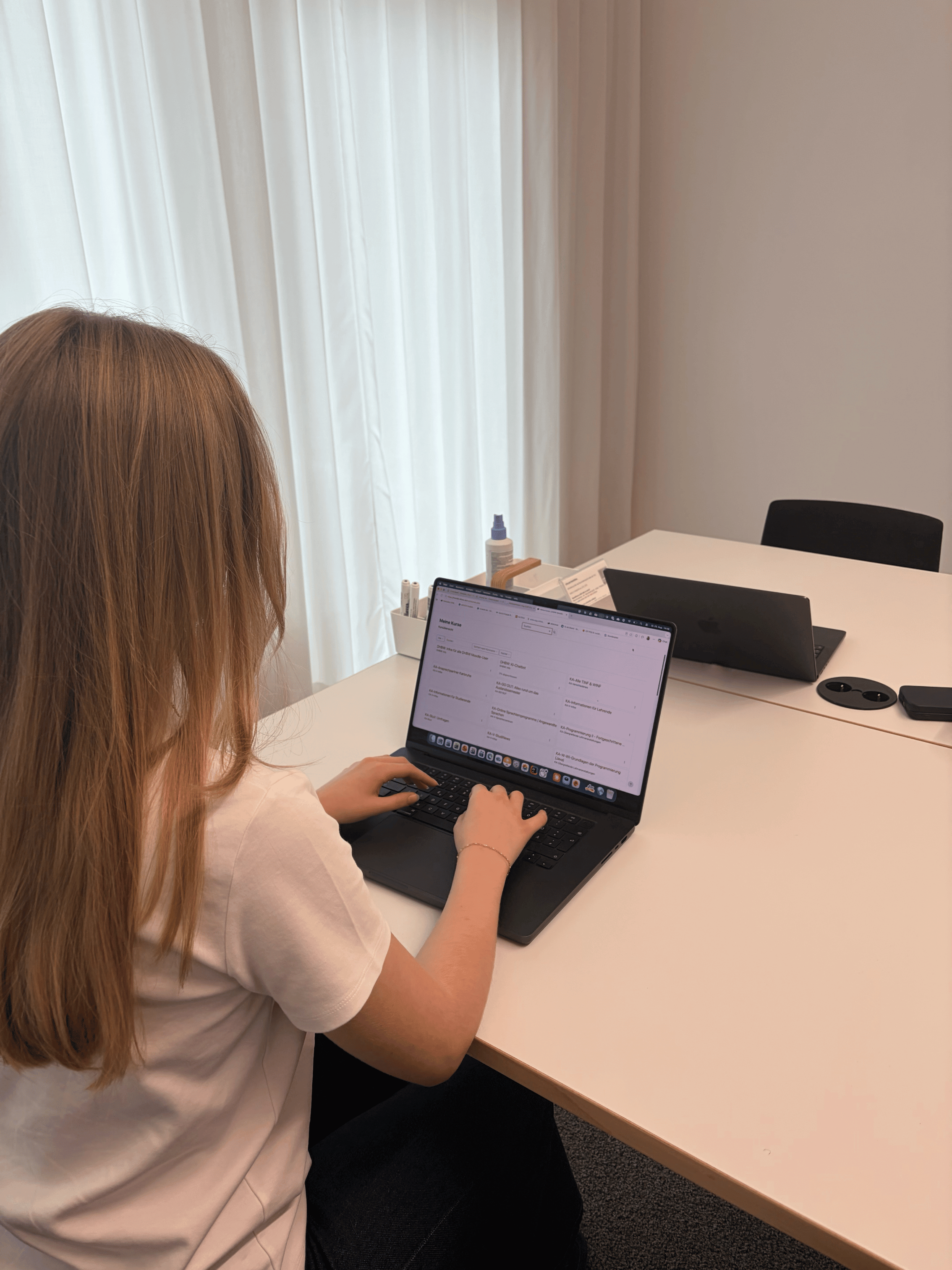 Eine duale Studentin sitzt mit dem Rücken zur Kamera und tippt auf einem Laptop, der einen Kursplan anzeigt