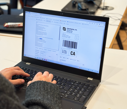 Auf einem Laptop ist die Druckvorlage eines Etiketts zu sehen, die von einer Person bearbeitet wird.