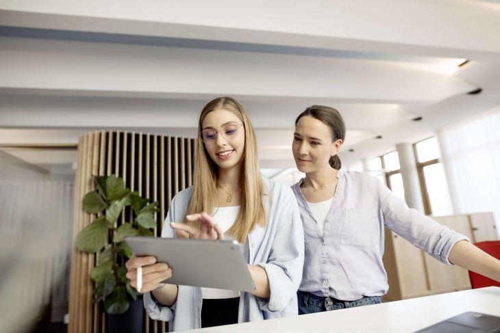 dmTECH-Praktikantin und Kollegin arbeiten gemeinsam am iPad.