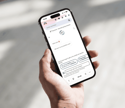 Eine Hand hält ein Smartphone auf dem der digitale Assistent dmKI im dm Onlineshop geöffnet ist