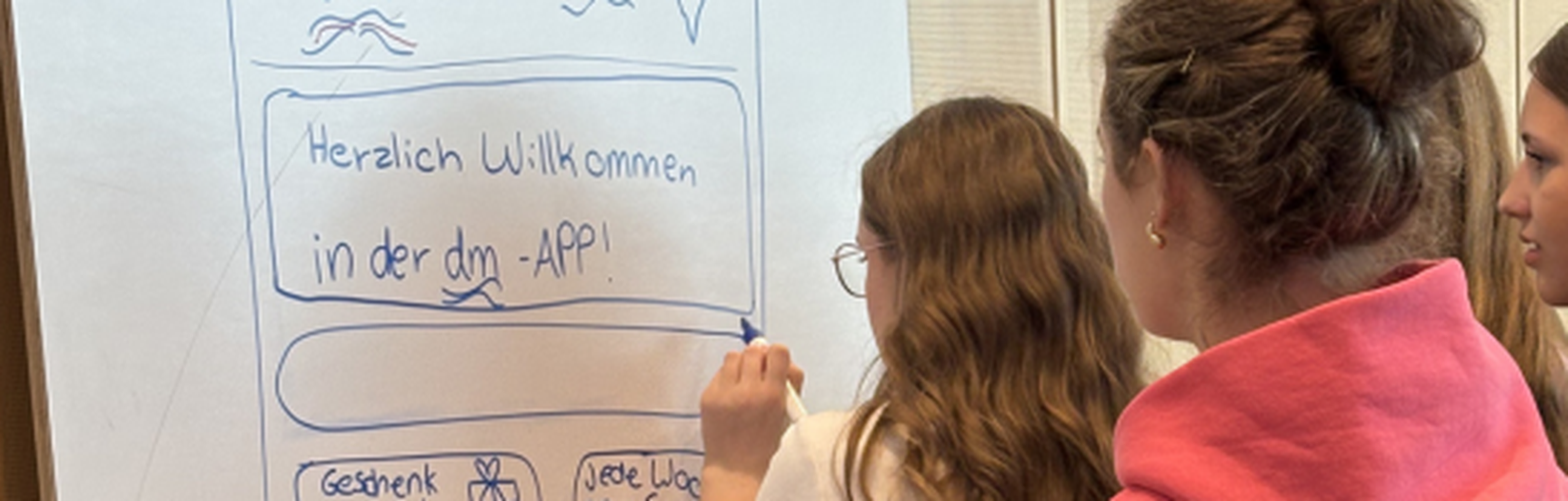 Zwei Schülerinnen des Girls Day bei dmTECH stehen mit dem Rücken zur Kamera und gestalten auf einem Whiteboard neue Vorschläge für die dmApp.