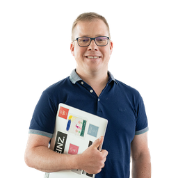 Junger Mann mit Brille und Laptop im Arm lächelt