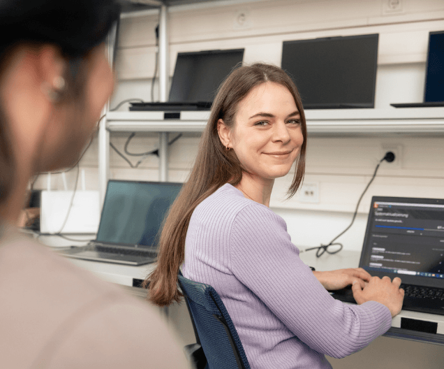 IT-Administratorin sitzt vor aufgeklapptem Laptop und lächelt in die Kamera