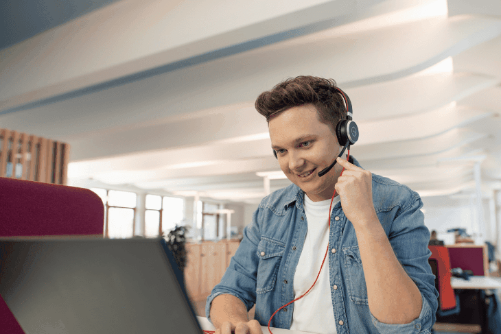 Auszubildender mit Headset vor Laptop in Open-Space-Büro im dm-dalogicum