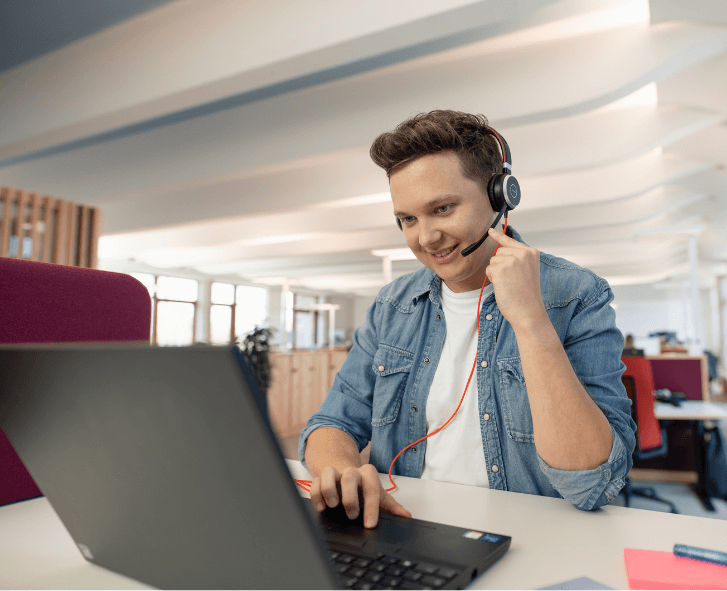 Auszubildender mit Headset vor Laptop in Open-Space-Büro im dm-dalogicum